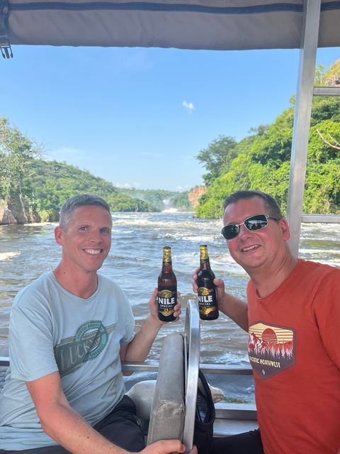 Two men holding drinks with a waterfall in the background.
