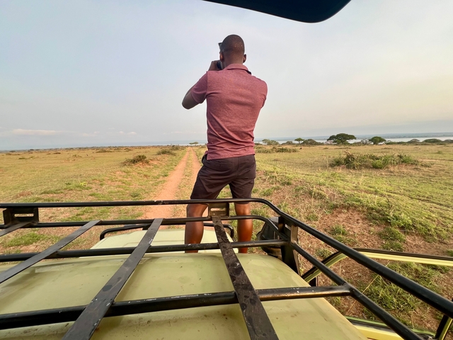 Person standing on a vehicle taking photos of the savannah.