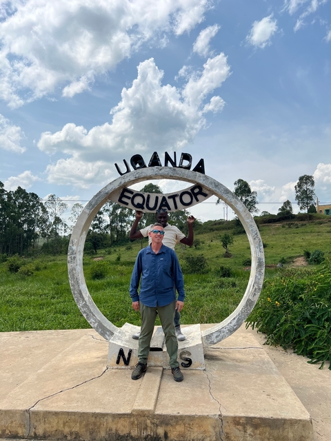 Two people posing beneath a sign marking the equator in Uganda.