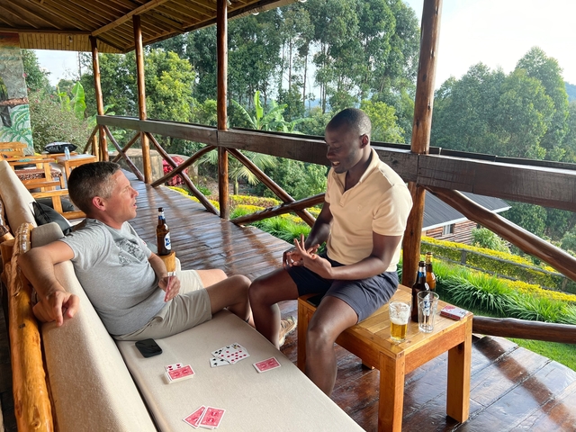 Two men playing cards on a veranda with drinks.