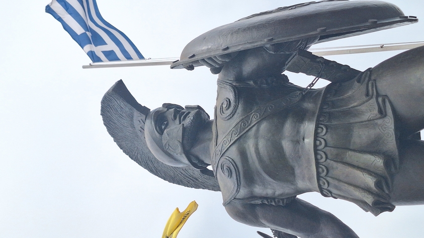       Close-up of a statue warrior with Greek flag.
  