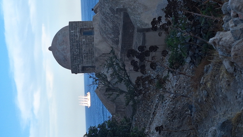       Stone building with a view of the sea and a sailing ship.
  