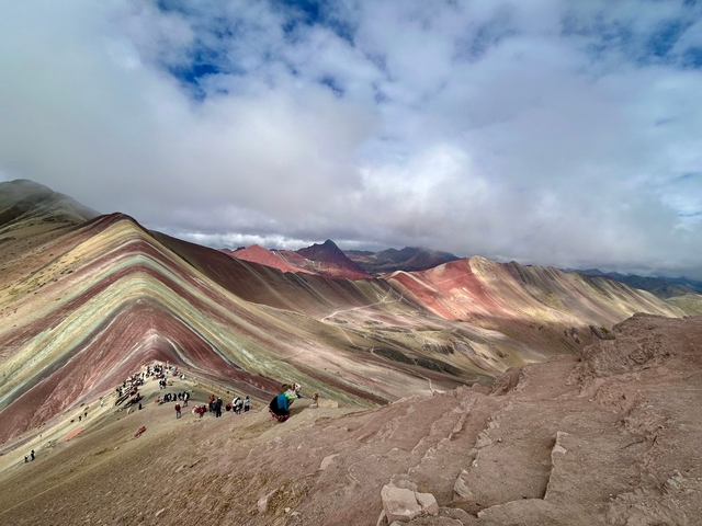      People hiking on Rainbow Mountain with vibrant colors and a mountainous background.
  