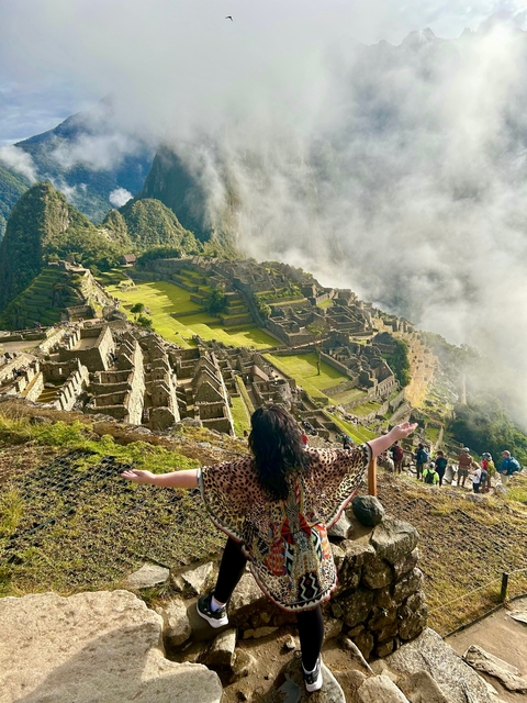       A woman with open arms overlooking Machu Picchu.
  