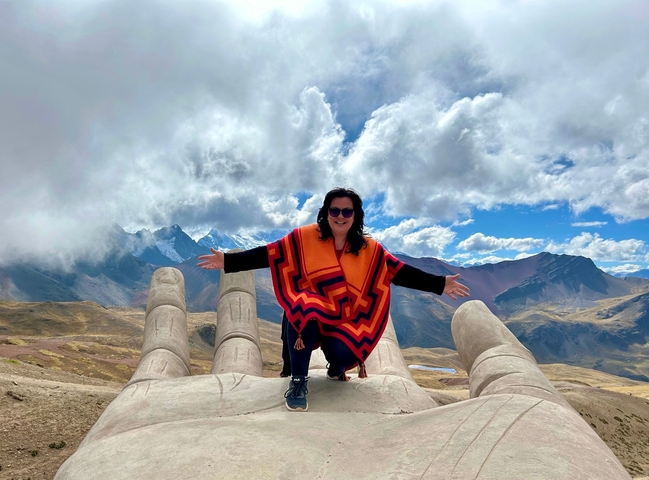       A person standing on a sculpture of a giant hand with mountains in the background.
  