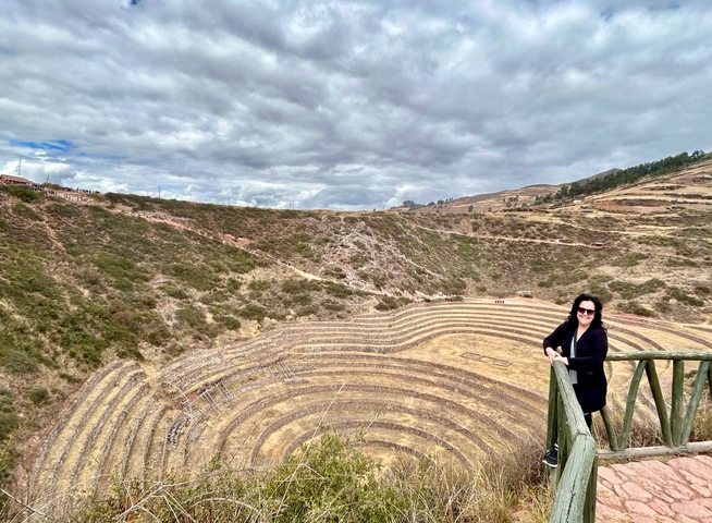       A woman overlooking the circular agricultural terraces of Moray.
  