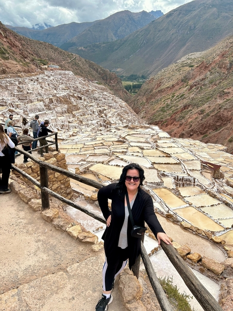       A woman posing at the Maras salt ponds in Peru with people in the background.
  