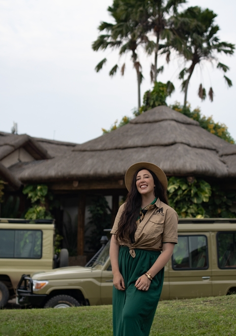 Woman wearing a safari hat smiling in front of thatched roof structures.