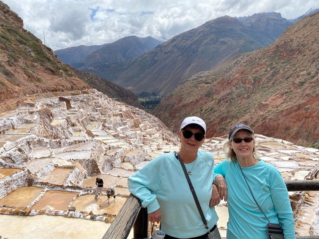       Two women posing in front of Maras Salt Mines with a scenic mountainous backdrop.
  