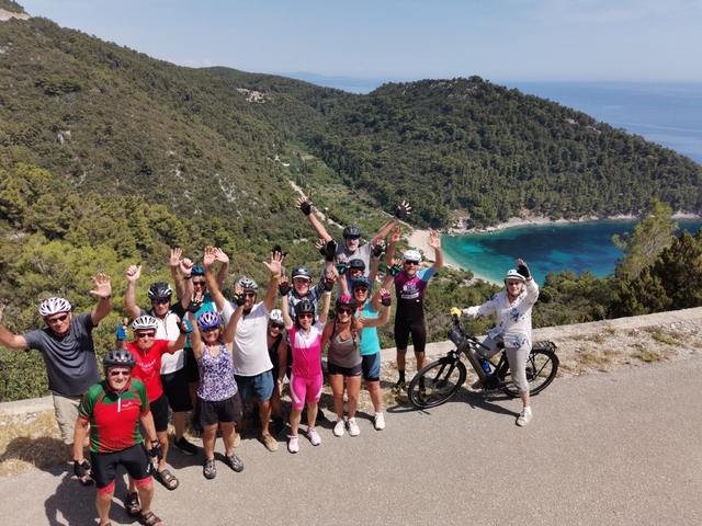       Group of cyclists posing with scenic coastal backdrop.
  
