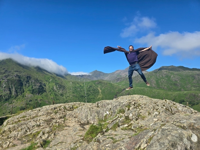 Man jumping on rocky terrain with mountains in the background.