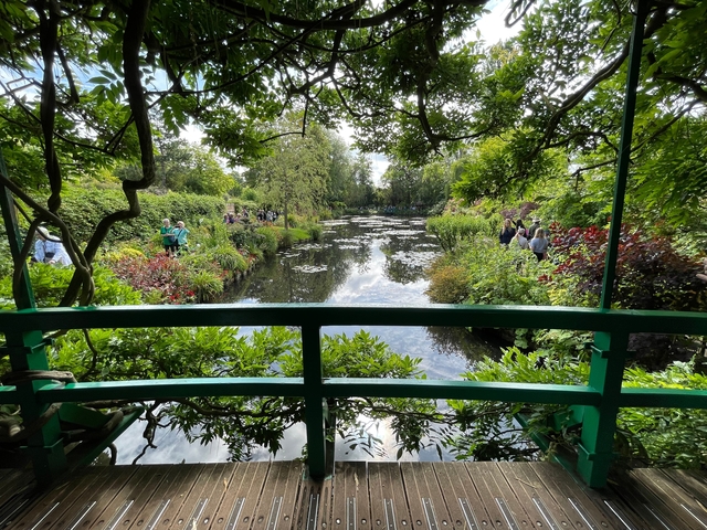       Serene pond with a bridge and lush gardens, inspired by Monet.
  