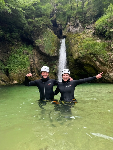 Couple in wetsuits posing in front of a waterfall.