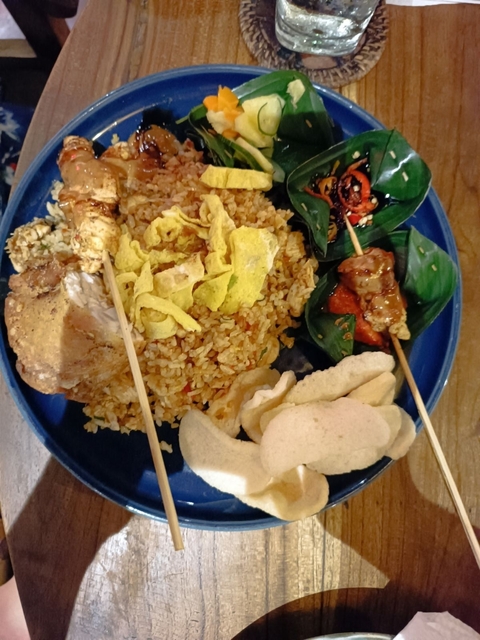 Plate of traditional Indonesian food with rice and skewers.