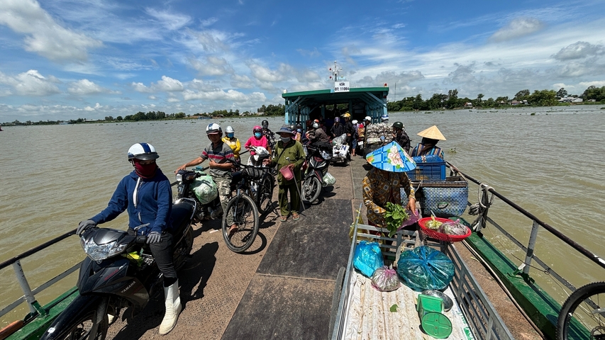       People with motorbikes on a ferry crossing a river.
  