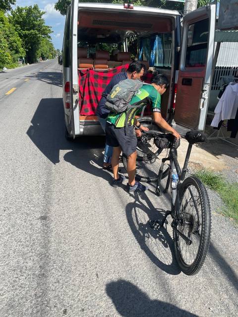 Cyclists adjusting their bikes beside a van.