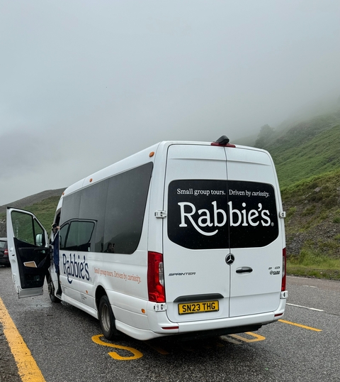 Small group tour vehicle with branding parked in a scenic area.