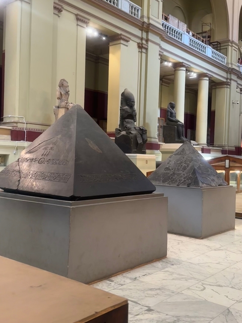       Museum with two black pyramidal artifacts on display.
  