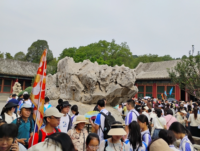       Crowd of people in an outdoor cultural site with a large rock.
  