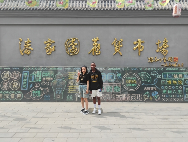      Two people posing in front of a wall with decorative text.
  
