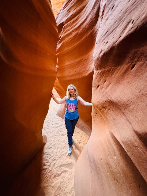 Woman standing between narrow red sandstone canyon walls.