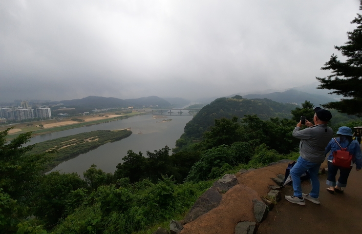       Tourists overlooking a misty river valley with a bridge.
  