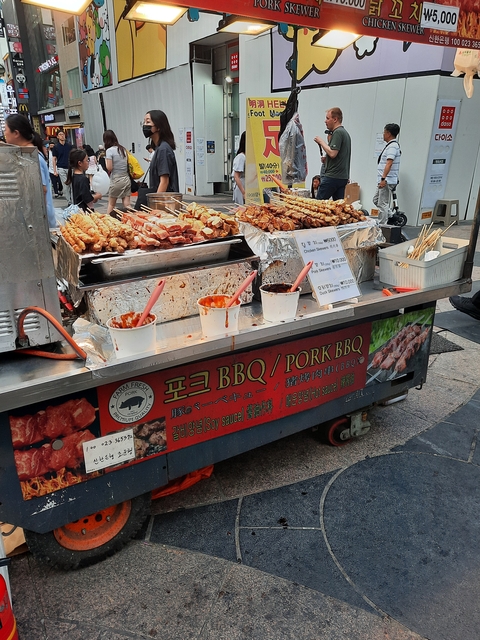 Street food vendor selling grilled skewers with dipping sauces.