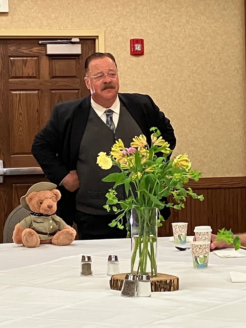 A person standing behind a table with flowers and a teddy bear.
