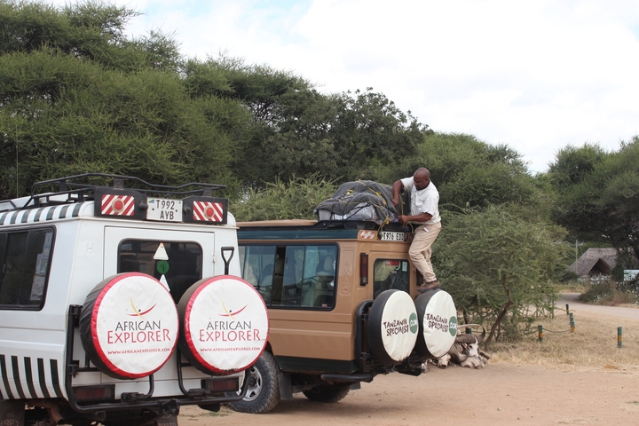       A person securing luggage on top of a safari vehicle.
  