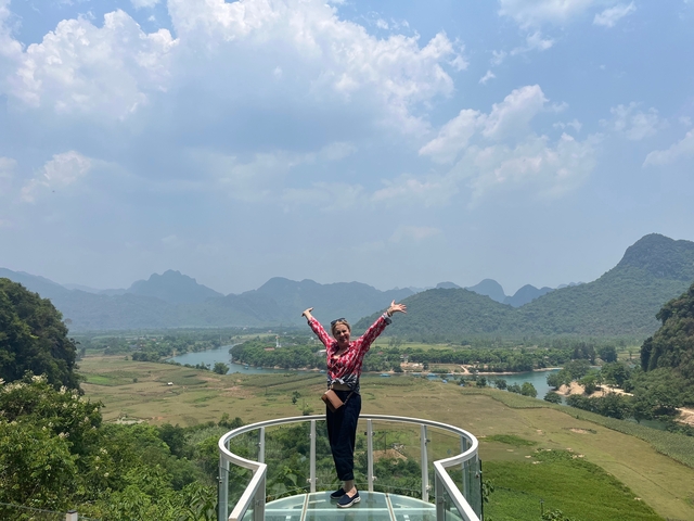 Person joyfully posing on an observation platform with a river and mountains in the background.