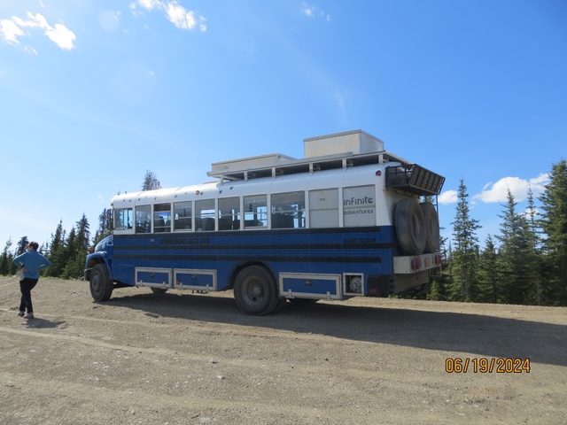       Tour bus parked on a dirt road with trees in the background.
  