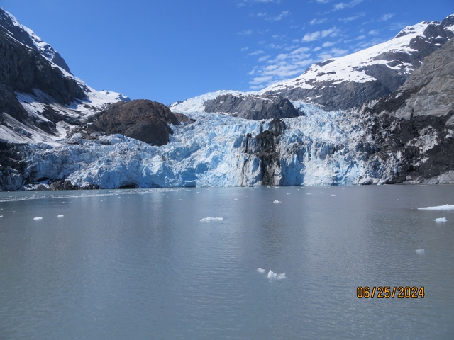       Glacier flowing into a calm body of water, snow-covered peaks.
  