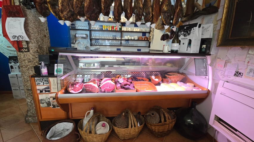 Interior of a deli with meat display and hanging cured meats.