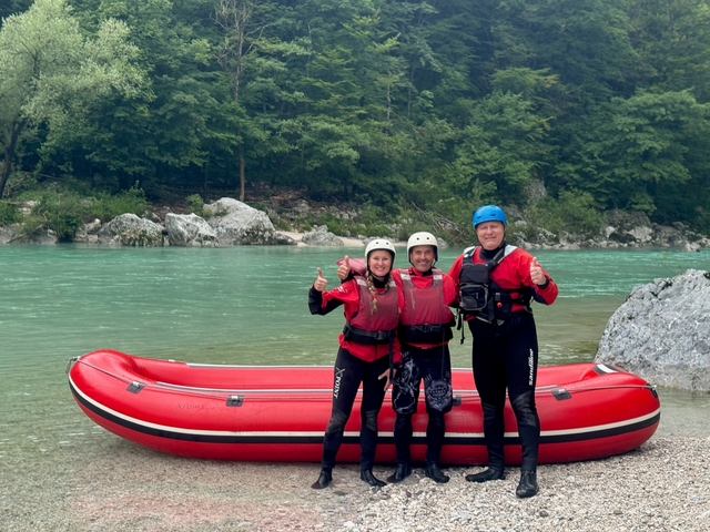       Three people posing with thumbs up by a red raft.
  