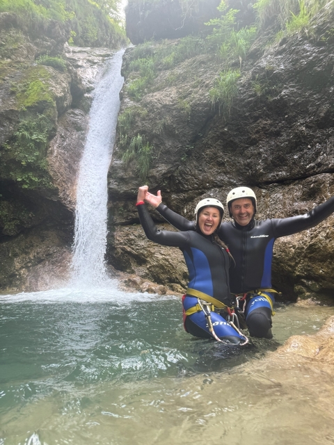       Two people in wetsuits celebrating by a waterfall.
  