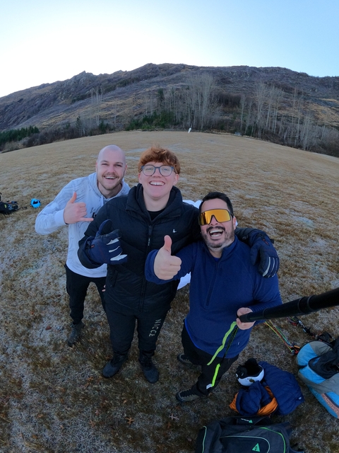 Three people posing on an open field with smiles.