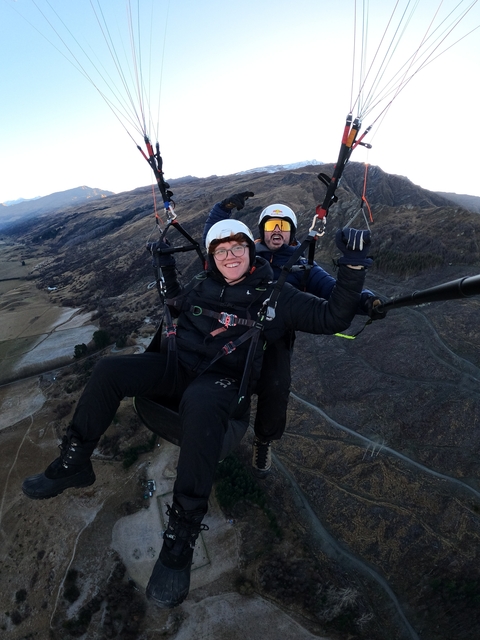 Two people paragliding over open landscapes.