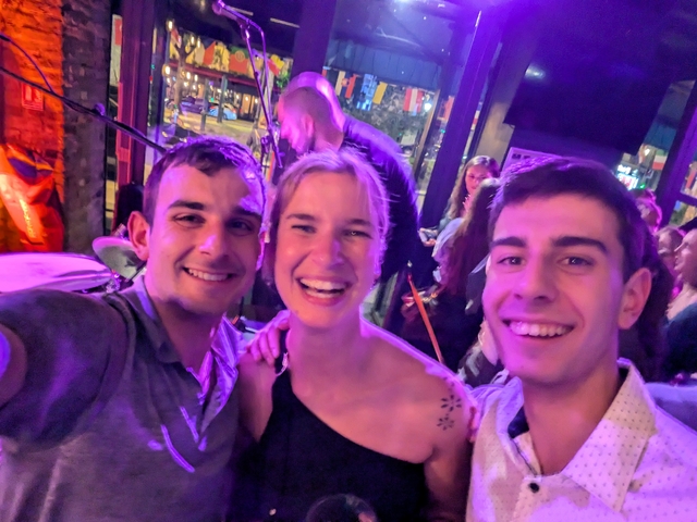 Three people smiling in a lively indoor setting.