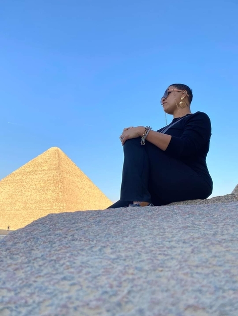 A person sitting on a rock with a pyramid in the background.