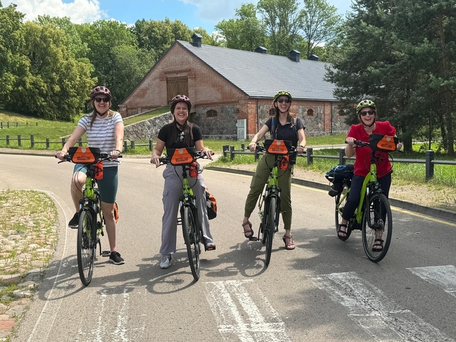 Four people on bicycles posing in front of a historic brick building.