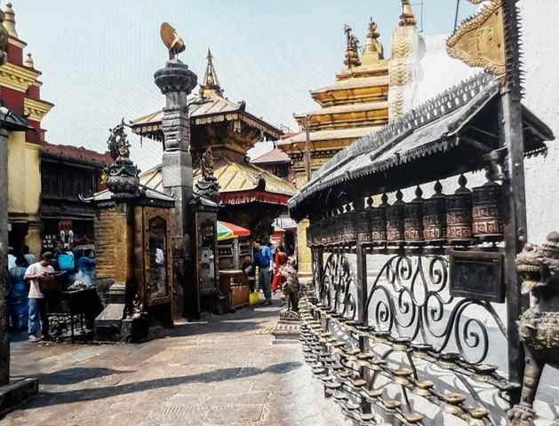 People at a temple with prayer wheels and traditional architecture.