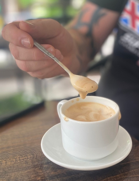Cup of coffee with a spoon held above it.