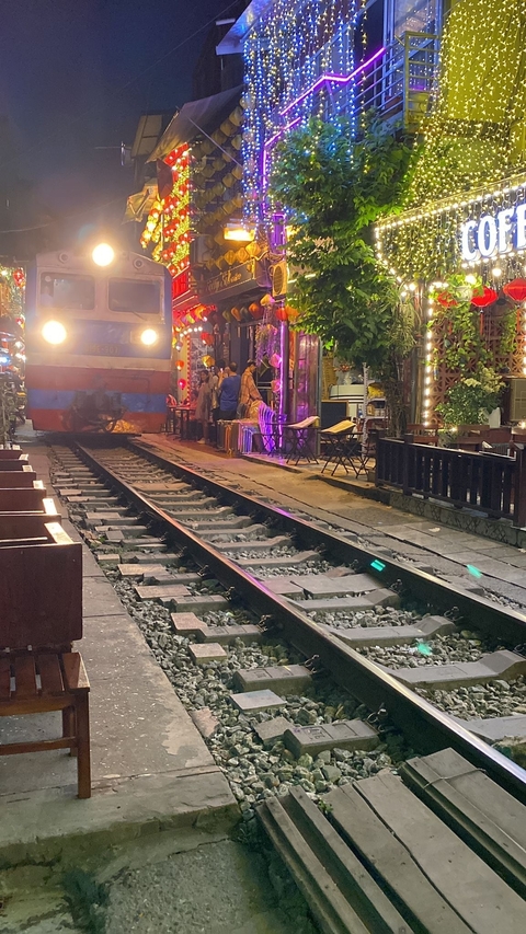 Train passing through a lively street with cafes at night.