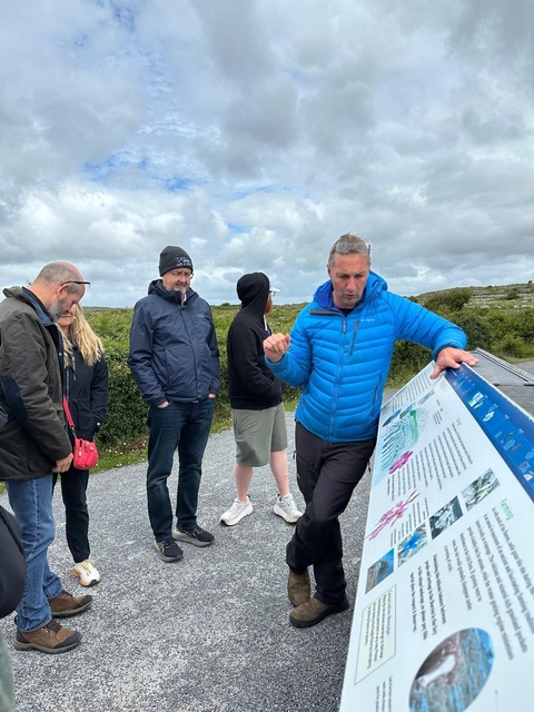 Man explaining information at an outdoor sign with a group of people.
