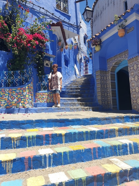       A person posing on a colorful staircase in a blue painted town.
  