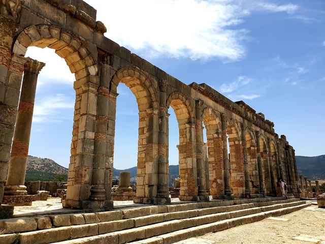       Large ancient ruins with multiple arches under a partly cloudy sky.
  