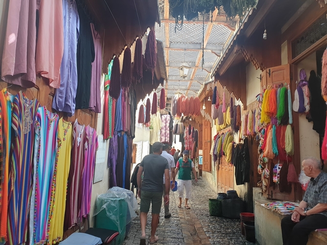       Busy market with colorful fabrics on display in a narrow alley.
  