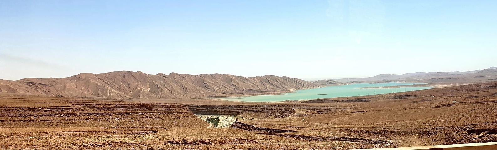Desert landscape with a turquoise lake under a clear sky.