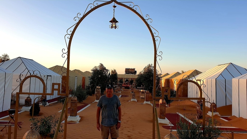       Tourist standing at a desert campsite with ornate tents.
  