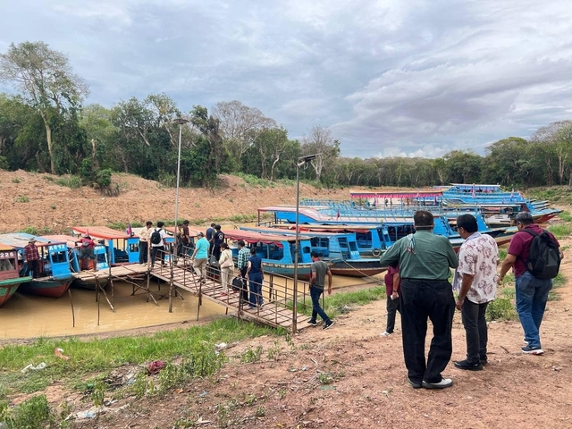 People boarding colorful boats at a riverbank, surrounded by lush greenery.